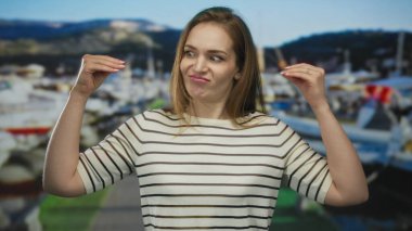 Beyaz çizgili tişörtlü beyaz bir kadın deniz kenarında el hareketleriyle konuşuyor. Hayal kırıklığı..