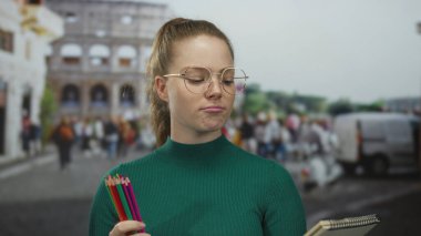Kadim kolezyumun yanında elinde renkli kalemler tutan gözlüklü genç bir kadın. Yaratıcı bir düşünce..