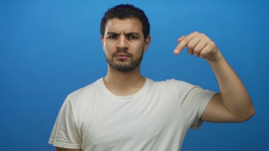 Genç ispanyol adam ciddi bir ifadeyle izole edilmiş mavi stüdyoda somurtkan suratını işaret ediyor..