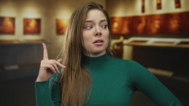 Modern müzedeki sanat eserlerini işaret eden ve kulağına dokunan kadın, merak yansıması.