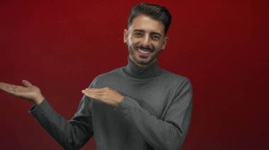 Erkek, sunum için kırmızı bir stüdyo duvarına karşı çıplak avuçlar ve davetkar bir gülümseme sunar..