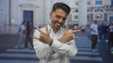 İspanyol adam, kalabalık bir şehir geçidinde iki eliyle kaya boynuzları hareketi sunuyor; eğlence enerjisi.