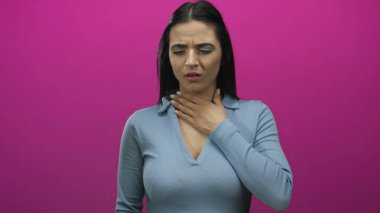 Mavi gömlekli İspanyol kadın kendini iyi hissetmiyor ve boğazını pembe bir arka plana yaslıyor. Hastalık ya da rahatsızlığı gösteriyor..