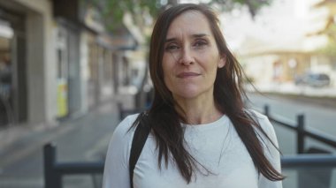 Şehir caddesinde gezen kadın rüzgar saçlarını savururken düşünceli görünüyor. Şehir ortamında huzurlu bir an yaşanıyor..