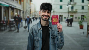 Şehir caddesinde elinde İngiliz pasaportuyla gülümseyen bir adam, sıradan şehir arka planıyla kot ceket giyiyor, seyahat hazırlığı ve açık hava yaşam tarzı sergiliyor..