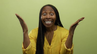 Sarı gömlekli, sarı bir duvara karşı şaşırdığını ifade eden örgülü bir kadın stüdyo ortamında canlı duygular ve saç stili sergiliyor..