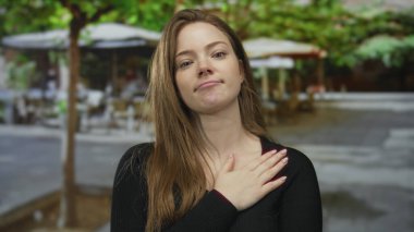 Kafkasyalı genç bir kadın açık hava restoranının terasına elini koyuyor bulanık masalar ve şemsiyelerle; samimiyet.