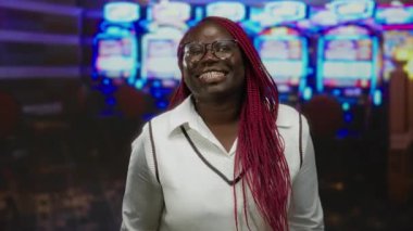 Kumar makinelerinin önünde kumarhaneden hoşlanan bir kadın neşeli bir ifade takınıyor, gözlük takıyor ve beyaz bir kazak giyiyor, açık havada canlı bir atmosferi ön plana çıkarıyor..