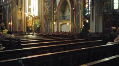 Oturan figürlerle dolu bulanık, renkli, süslü bir Katolik kilisesinin içindeki sıralar kilisenin canlı mimarisini ve ortam aydınlatmasını gözler önüne seriyor..