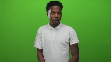 Beyaz polo tişörtlü bir adam yeşil ekran stüdyosunda duruyor ve doğrudan kameraya bakıyor..