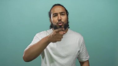 Adam, düz beyaz tişört giyen, tepe arkaplanına karşı stüdyoda doğrudan kameraya işaret eder; öfke yüzleşmesi.