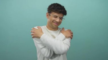 Gözlüklü ve beyaz süveter giyen İspanyol genç adam stüdyoda omuzlarına sarılıyor..