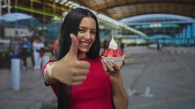 Gülümseyen kadın, havaalanında açık havada elinde dondurmayla gezintiyi ve boş zamanlarını resmeden parlak terminal geçmişiyle baş parmak kaldırıyor..