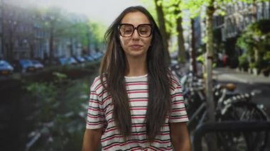 Büyük gözlük takan, gülümseyen ve saçlarını düzelten bir kadın Amsterdam caddesinde, kaygısız bir neşe.