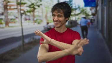 Kırmızı gömlekli adam yoğun şehir caddesinde coşkuyla el sallıyor ve gülümsüyor..