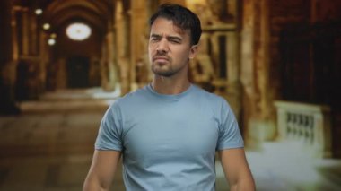 Kilisenin içinde hayal kırıklığını ifade eden, sıradan kıyafetler giyen ve loş bir katedralde el kol hareketi yapan genç bir adam..