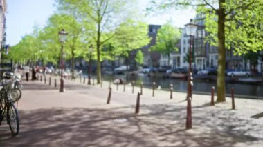 Ağaçların, bisikletlerin, kanalların olduğu bulanık bir manzara. Ve noktalı güneş ışığı altında, Hollanda yolunda yürüyen odaksız insanlar..