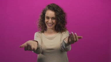 Genç İspanyol kadın gülümseyen ve iki eliyle işaret eden eflatun stüdyo; neşeli karşılama daveti.