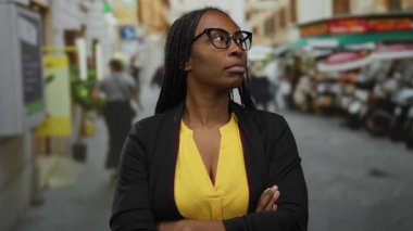 Şehir merkezinde kendine güvenen bir kadın, gözlük takıyor ve şehir arka planında bulanık sarı bir bluz giyiyor.