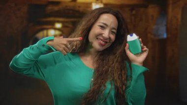 Kadın, eski binada yeşil astım cihazını tutarken yanak yanağa işaret ediyor; ürün gösterişli.