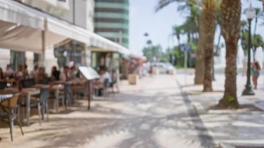 Güneşli bir günde, arka planı çözülmüş, avuç içi çizgileri üzerinde yürüyen insanların oturduğu bulanık bir açık kafe..