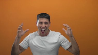 Genç İspanyol adam stüdyoda yumruklarını sıkıyor ve kameraya turuncu arka planla bağırıyor; öfke.