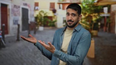 Açık havada genç bir adam büyüleyici bir şehir sokağında ellerini uzatırken bir şaşkınlık ifadesi sergiliyor, canlı bir şehir zeminine karşı kurulmuş, gün ışığında rahat bir cazibe yayıyor..