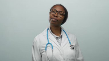 Steteskoplu beyaz önlüklü kadın beyaz arka planda poz veriyor. Yükseltilmiş yumruğu ve sakin ifadesiyle sağlık ortamında güven ve profesyonellik gösteriyor.