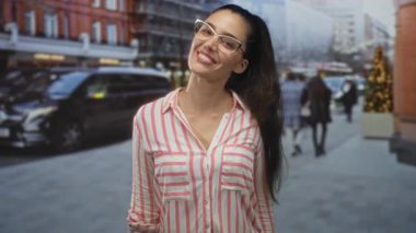 Gözlüklü ve pembe çizgili tişörtlü genç İspanyol kadın sokaklarda olumlu jest yapıyor; iyimserlik.