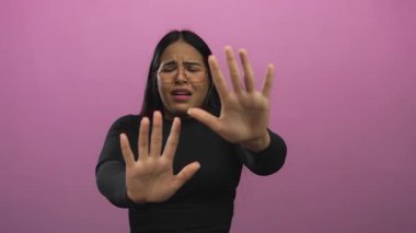 Kadın, genç Latin kökenli Latin 'in pembe arka planla tek başına yüzleştiği stüdyoda durmak için ellerini kaldırıyor..