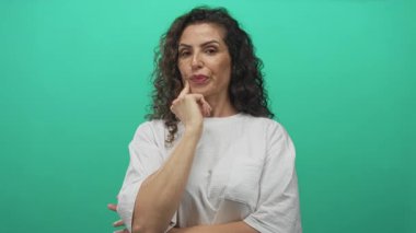 Kadın yeşil stüdyodaki işaret parmağıyla çeneye dokunur yumuşak ışık altında ayarlanır; düşünceli yansıma.