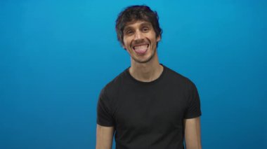 Dil hareketini gösteren canlı, mavi bir stüdyo duvarına dil uzatan genç adam..