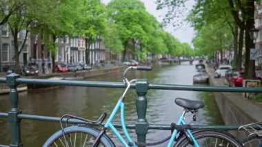 Arka planda yemyeşil ağaçlar ve tarihi binalarla dolu, sakin ve klasik şehir manzaralı bir köprü üzerindeki bisiklet..