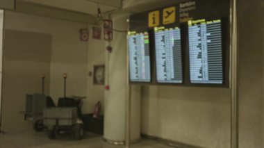 Bulanık havaalanı terminali ekranı kapalı bir odada uçuş bilgilerini gösterirken, bokeh etkisi ile panoyu ve çevreyi vurguluyor.