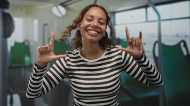 Çizgili bluzlu genç kadın gülümsüyor, eller şekilleniyor. Seni seviyorum. Sokakta bir otobüse imza at..