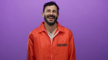 Turuncu hapishane tulumlu İspanyol sakallı bir adam mor bir arka plana karşı duruyor ve değişik duygular sergiliyor..