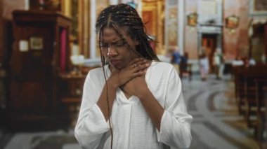 Kilise binasının içinde sıraların yanında dururken iki eliyle boğazını sıkan Afrikalı Amerikalı kadın. İnanç acıyla mücadele ediyor..