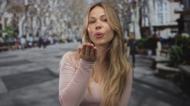 Çıplak ağaçların altındaki banklarla kaplı taştan kaldırımlara uzanan bir kadın pembe süveter giyerek öpüşüyor..