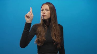 Stüdyoda, siyah gömlek ve uzun saç giyen, koyu mavi arka plana işaret eden bir kadın. Kararlılık..