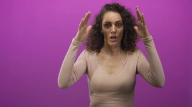 Mor stüdyoda elleri kulakları ve ağzı açık, kıvırcık saçlı genç İspanyol kadın. Sürpriz..
