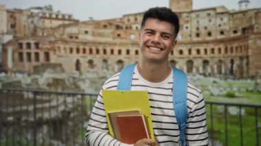 Gülümseyen adam eski harabelerin yanında kitap tutuyor.