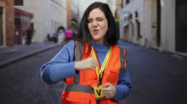 Turuncu yelekli esmer kadın, neşeli bir ifadeyle eski kasaba sokaklarında gönüllü olarak çalışıyor.