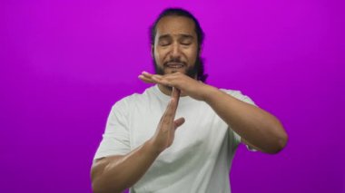 Elleri ve avuçları görünür halde, eflatun stüdyoda beyaz tişört giyen bir adam mola hareketi yapıyor; ciddi yansımayı duraklat.