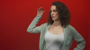 Tepeden tırnağa kadın, beyaz kolsuz bluz giyiyor ve kırmızı stüdyoda göğsünü gösteren katıksız yeşil gömlek; sessiz tefekkür.