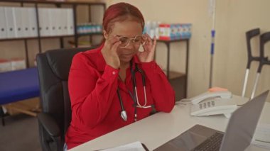 Steteskoplu kırmızı bluzlu kadın doktor, tıp binasında kulaklara dokunan gözlükleri ayarlar; yorgunluk.