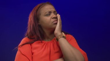 Turuncu bluzlu kadın, stüdyoda mavi ışıkta diş ağrısı için yanak tutuyor..