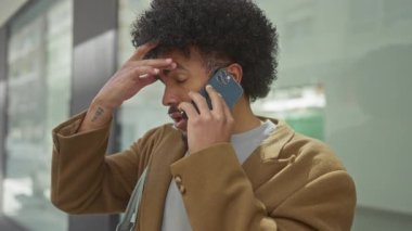 Şehir caddesinde akıllı telefondan birden fazla iş yapan Afrikalı Amerikalı bir adam yoğun bir ortamda odak ve düşünce karışımı sergiliyor..