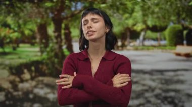 Kırmızı kazaklı İspanyol kadın, gün ışığında kollarını kavuşturur ve kaşlarını çatar. Gergin duruşuyla, öfke hüsranı meydan okumasıyla..