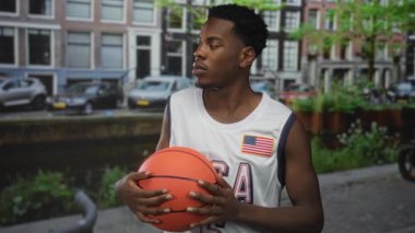 Şehir caddesinde, park etmiş arabaları ve tuğla binaları olan bir kanalda basketbol oynayan adam. Kararlılık..