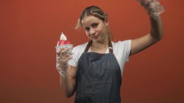 Elinde çilekli bir fincan dondurma tutan ve stüdyoda gözünün üstüne Ziyaretçi tabelası yapan bir kadın. Eğlenceli bir misafirperverlik..